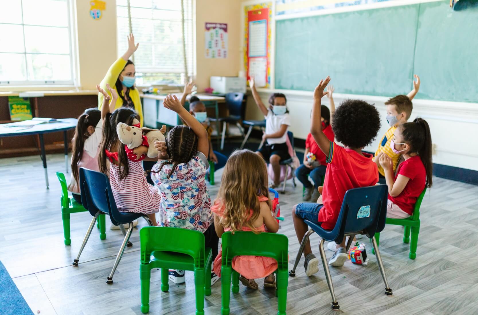 Lots of children sitting in a circle with their hands raised to get the teacher's attention