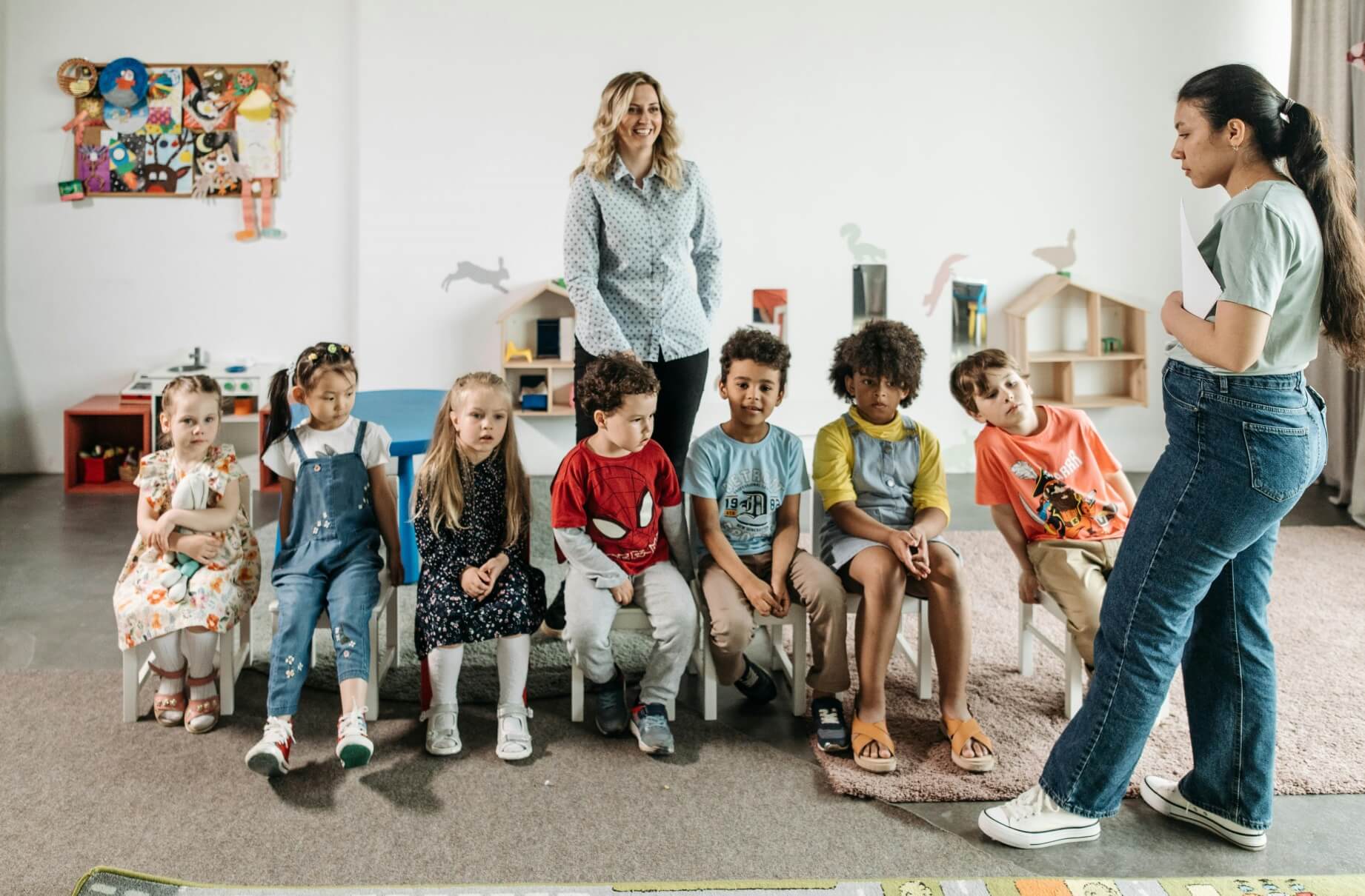 7 children sitting on chairs in a row and 2 teachers in a drama classroom