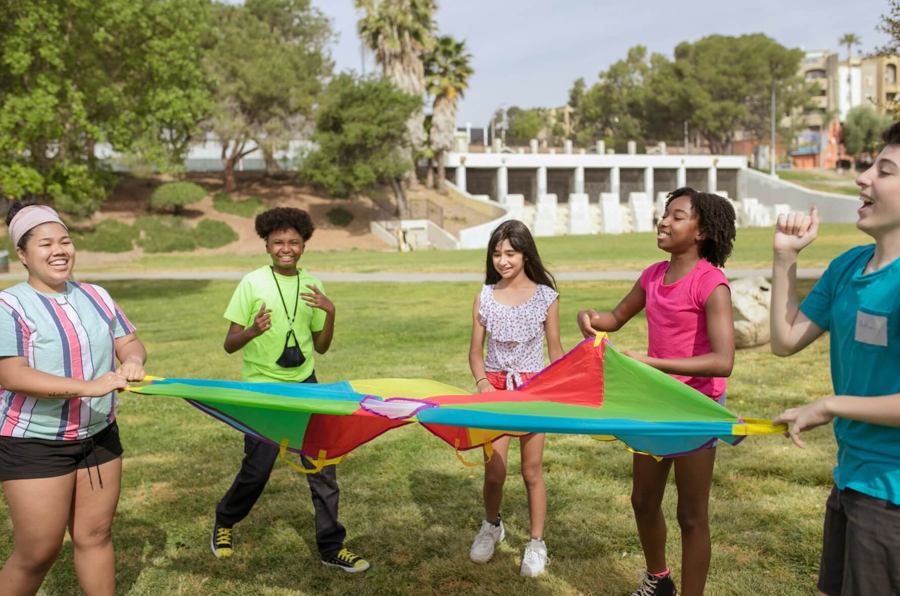 Children playing outdoors with a rainbow sheet