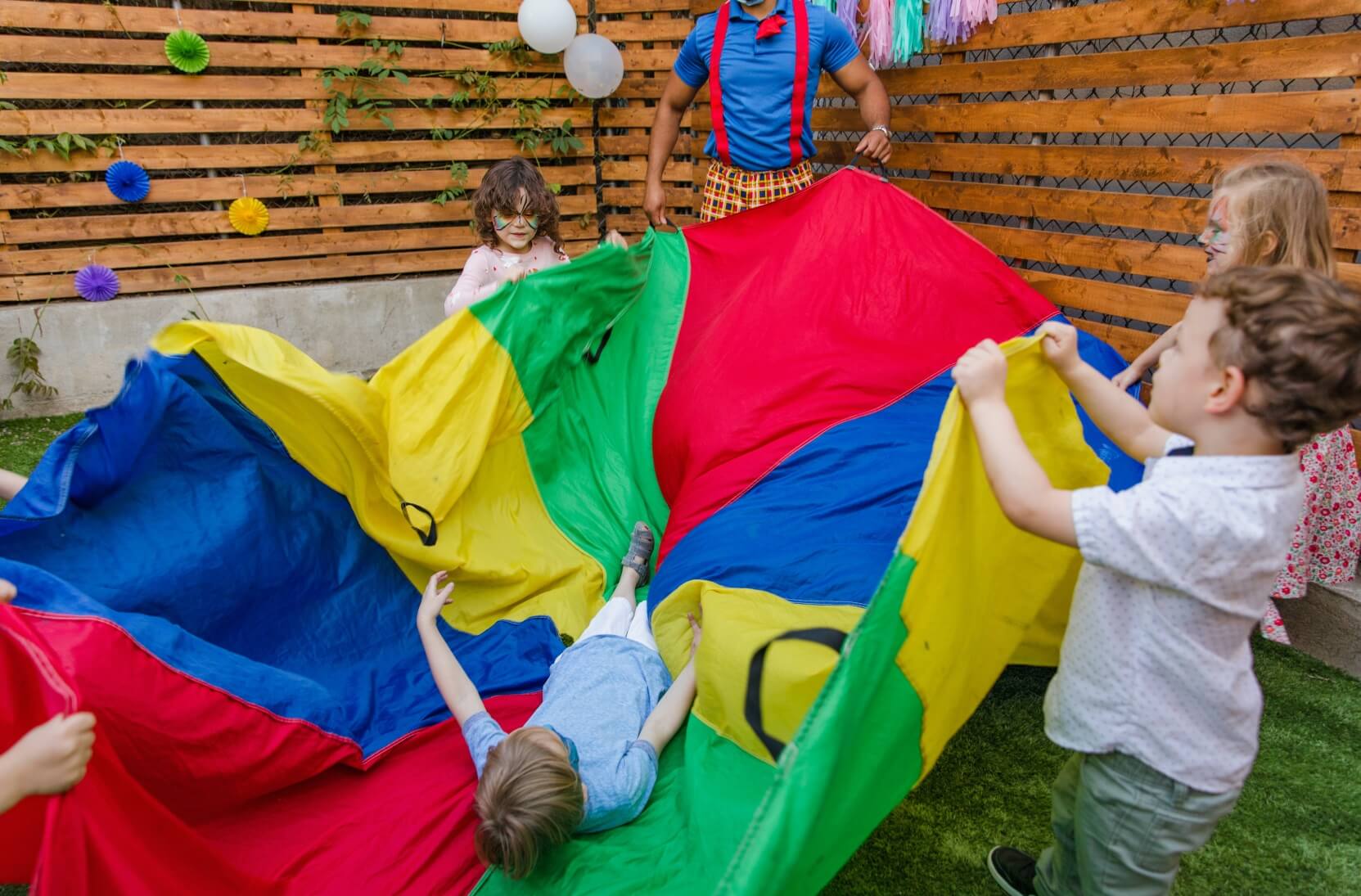 Children and an adult playing outdoors with a rainbow sheet